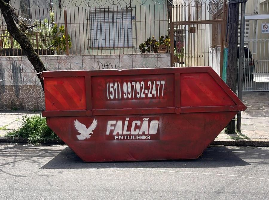 Caçamba vermelha da Falcão Entulhos estacionada na rua em frente a uma casa